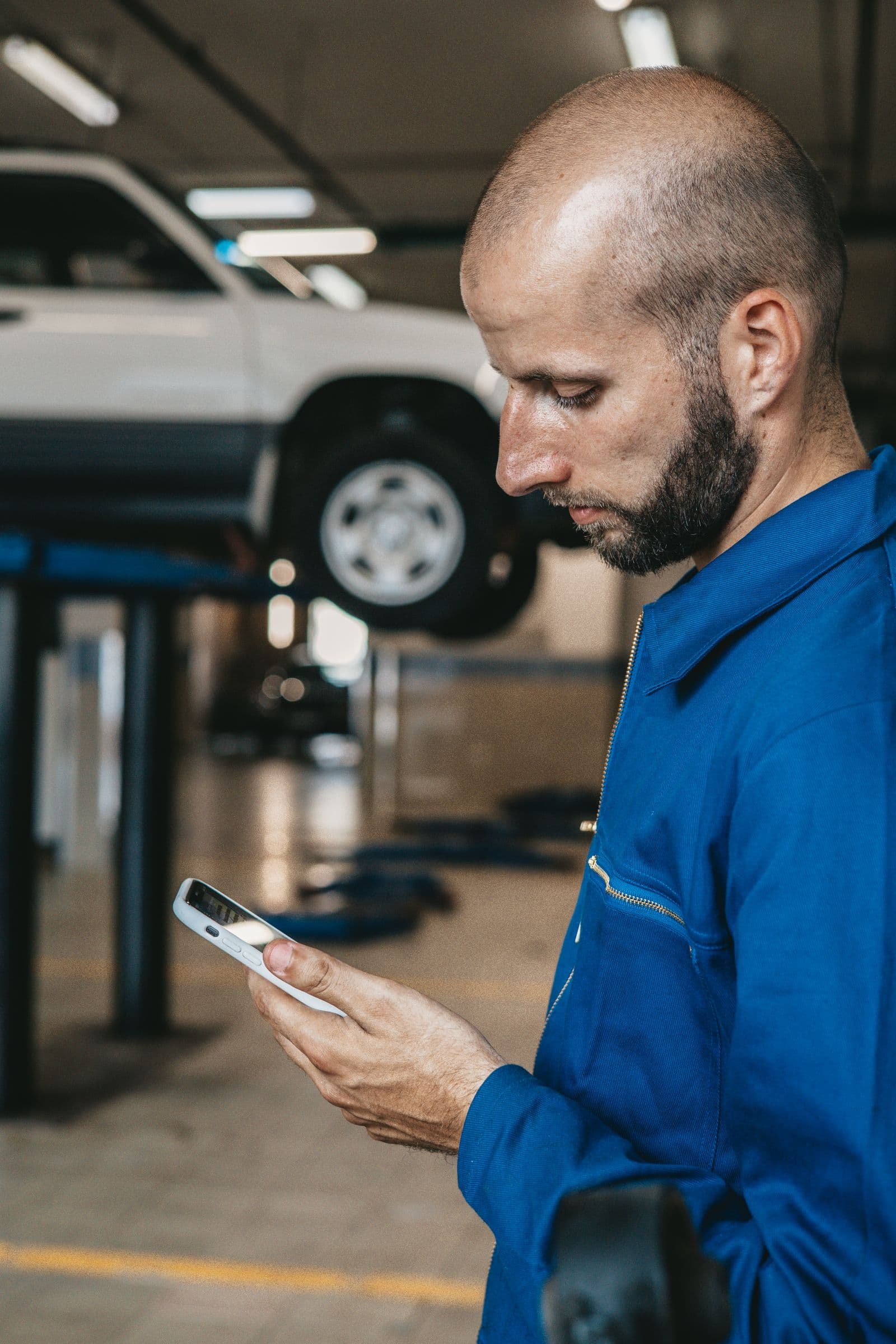 Oto serviste, liftteki aracın yanında telefonuna bakan bir çalışan